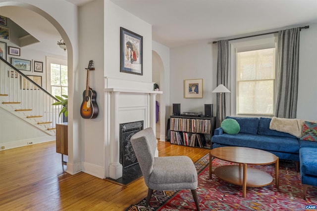 living area with arched walkways, light wood-style floors, a fireplace with flush hearth, and stairs
