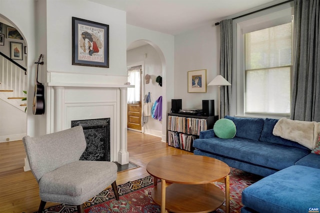 living room featuring arched walkways, wood finished floors, stairway, and a fireplace with flush hearth
