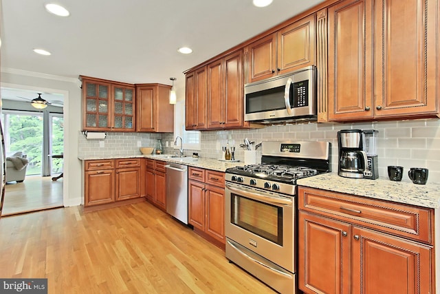 kitchen with stainless steel appliances, brown cabinetry, crown molding, light wood finished floors, and a ceiling fan