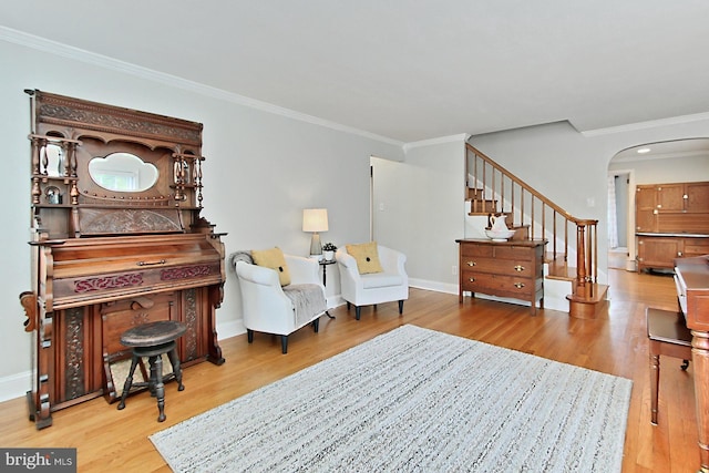 sitting room with arched walkways, wood finished floors, ornamental molding, stairs, and baseboards