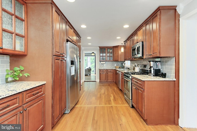 kitchen with appliances with stainless steel finishes, light wood-style flooring, tasteful backsplash, light stone counters, and recessed lighting