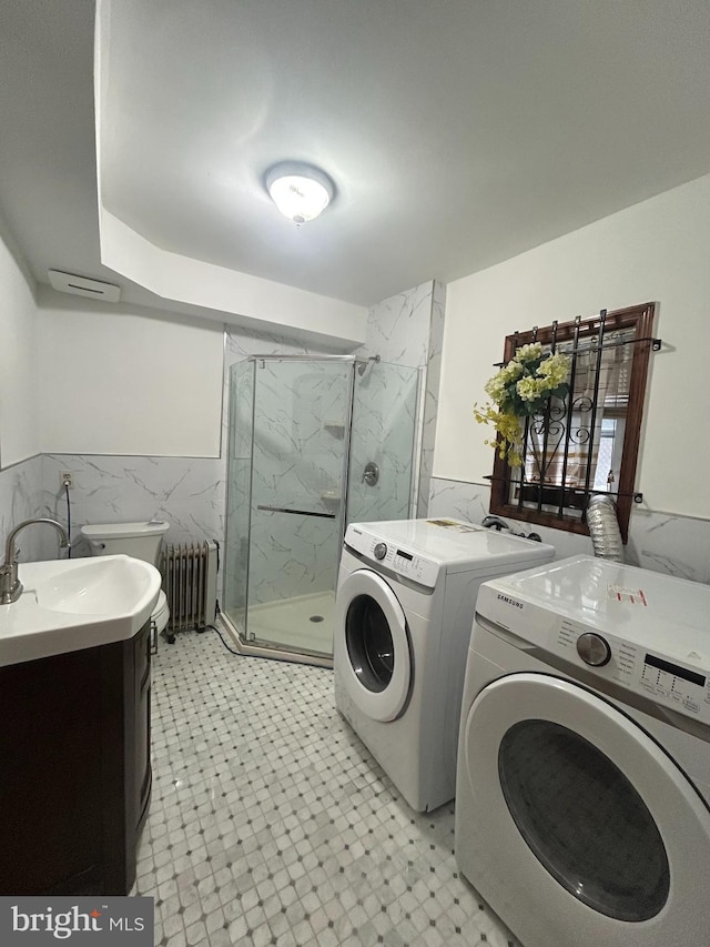 laundry room with radiator heating unit, independent washer and dryer, tile walls, light floors, and a wainscoted wall