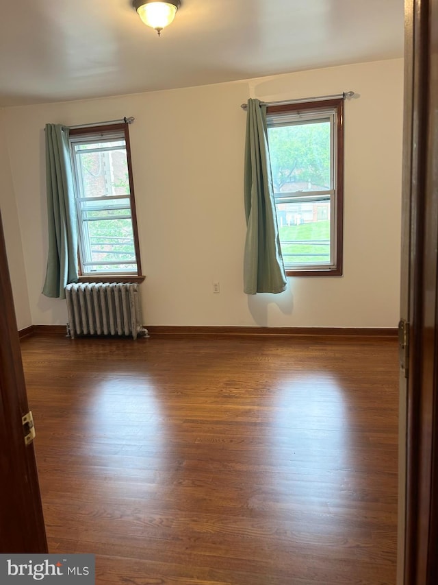 spare room featuring radiator, wood finished floors, and baseboards