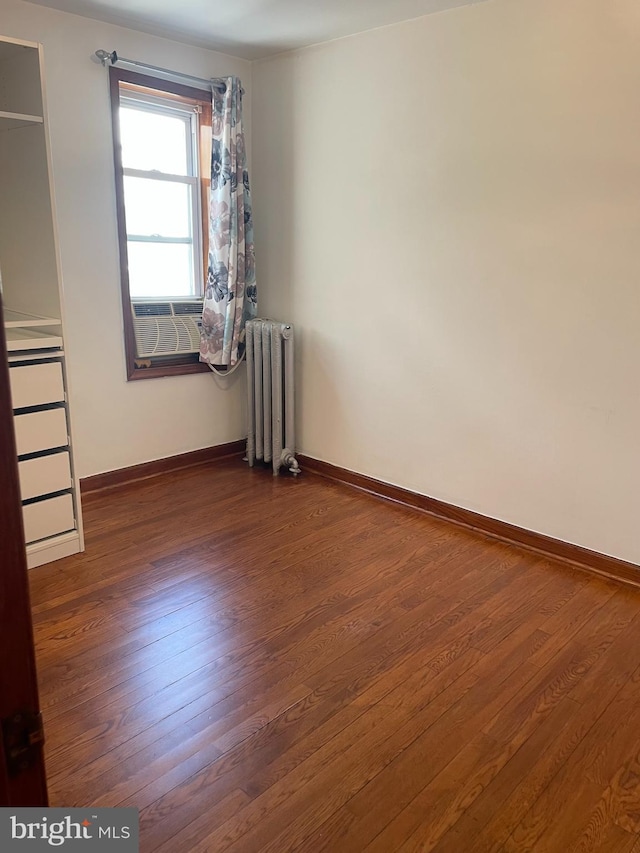 unfurnished bedroom featuring radiator, wood finished floors, and baseboards