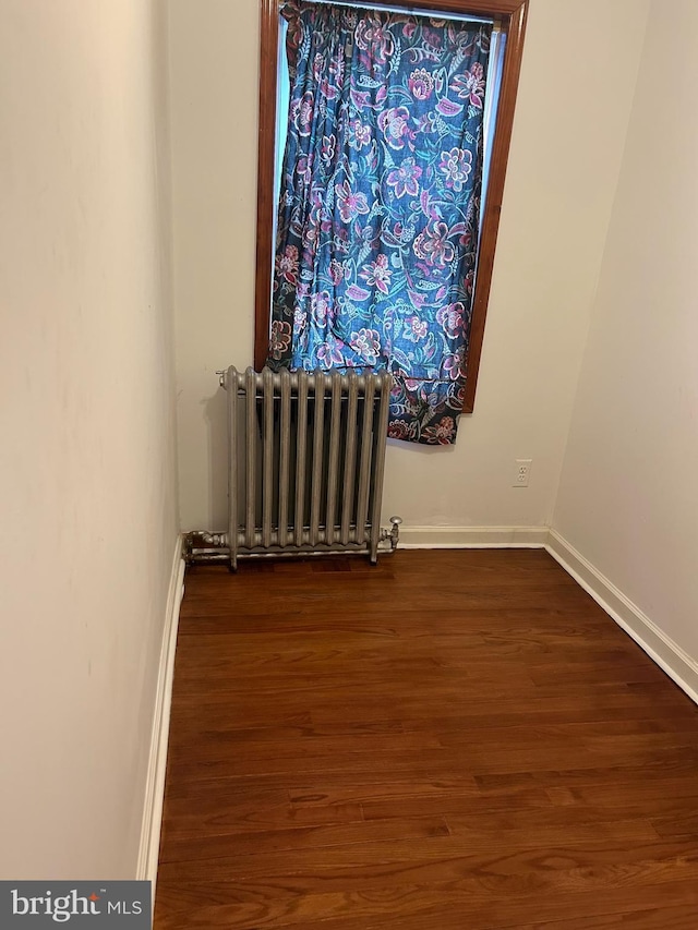empty room with radiator, dark wood-style flooring, and baseboards