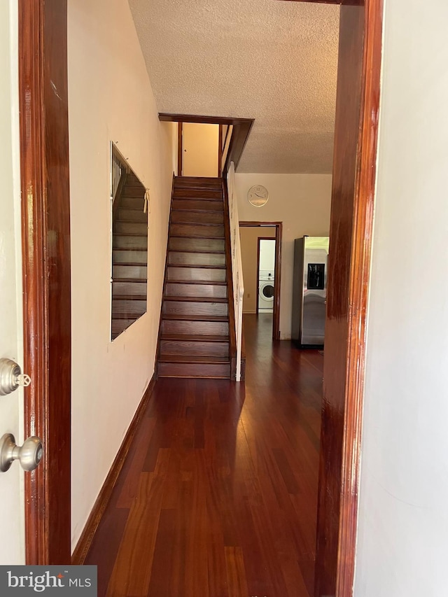 hall with washer / clothes dryer, stairway, a textured ceiling, wood finished floors, and baseboards