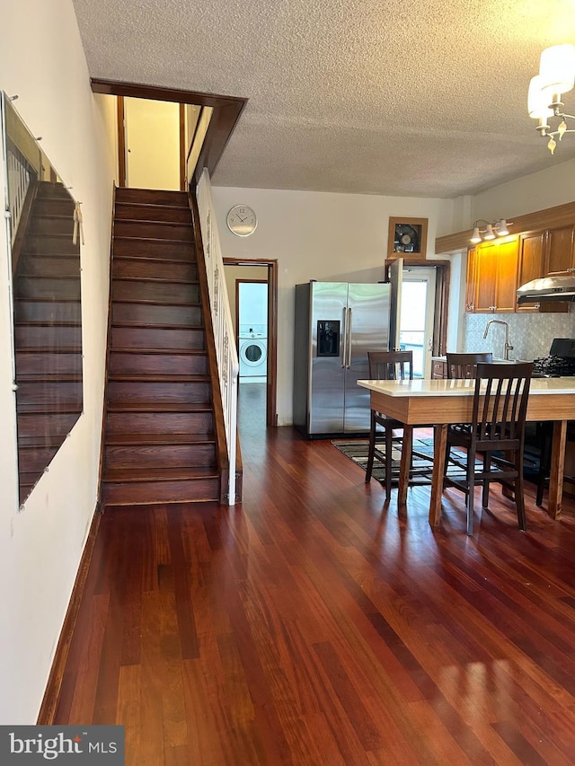 dining room featuring washer / dryer, a textured ceiling, stairs, a chandelier, and dark wood-style floors