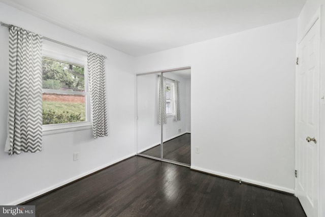 unfurnished bedroom featuring wood finished floors, multiple windows, a closet, and baseboards