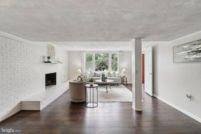 living area with hardwood / wood-style flooring, a textured ceiling, a brick fireplace, brick wall, and baseboards