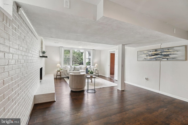 living area featuring hardwood / wood-style floors, a fireplace, baseboards, brick wall, and a textured ceiling