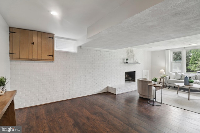 living room with dark wood finished floors, a brick fireplace, and brick wall