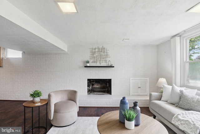living room featuring wood finished floors, brick wall, a textured ceiling, and a brick fireplace