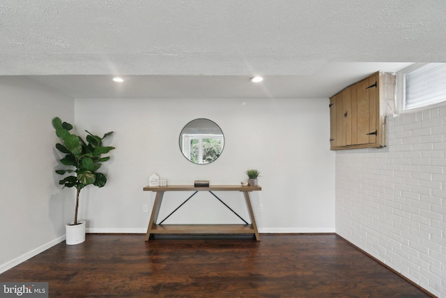 below grade area with a textured ceiling, wood finished floors, baseboards, recessed lighting, and brick wall