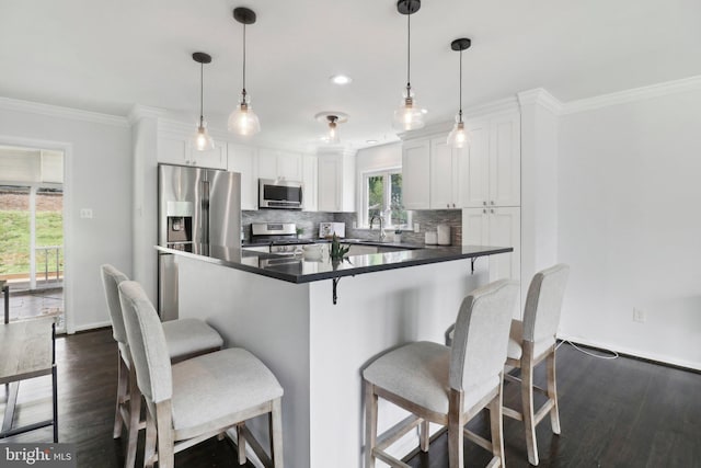 kitchen featuring appliances with stainless steel finishes, dark wood finished floors, white cabinetry, dark countertops, and ornamental molding