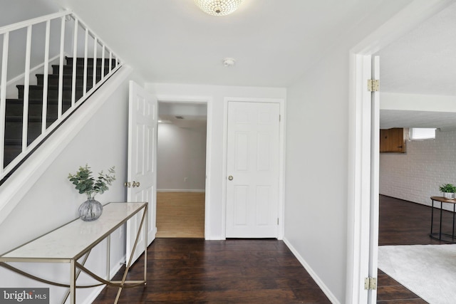 hall with dark wood-style floors, stairway, baseboards, and brick wall