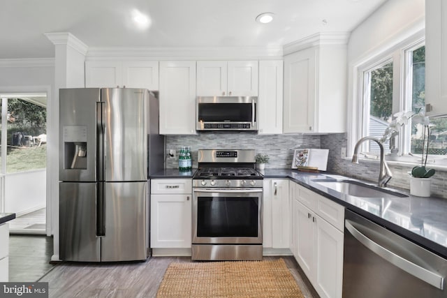 kitchen with stainless steel appliances, a sink, white cabinets, decorative backsplash, and ornamental molding