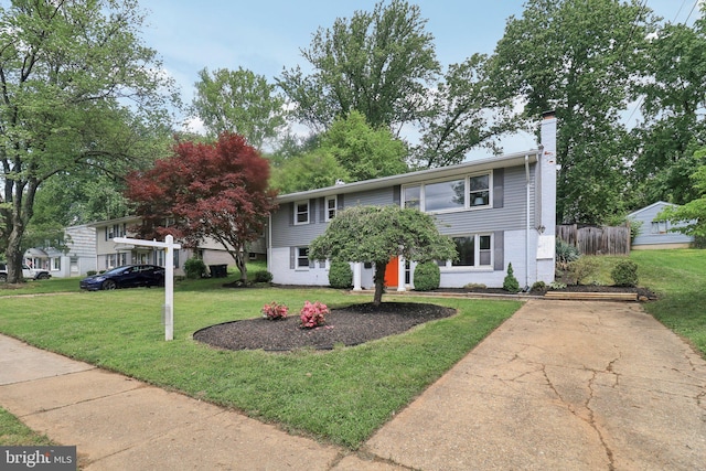 view of front of property featuring a front yard, a chimney, driveway, and brick siding