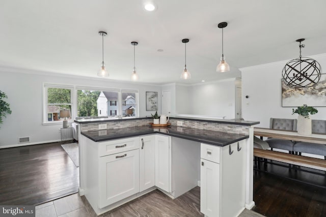 kitchen with dark countertops, ornamental molding, white cabinets, pendant lighting, and dark wood-style flooring