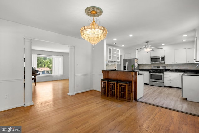 kitchen featuring stainless steel appliances, a breakfast bar area, dark countertops, white cabinets, and light wood-style floors
