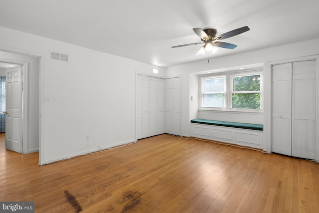 unfurnished bedroom with multiple closets, light wood-style floors, and ceiling fan