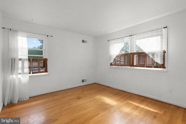 unfurnished room with wood finished floors, healthy amount of natural light, and baseboards