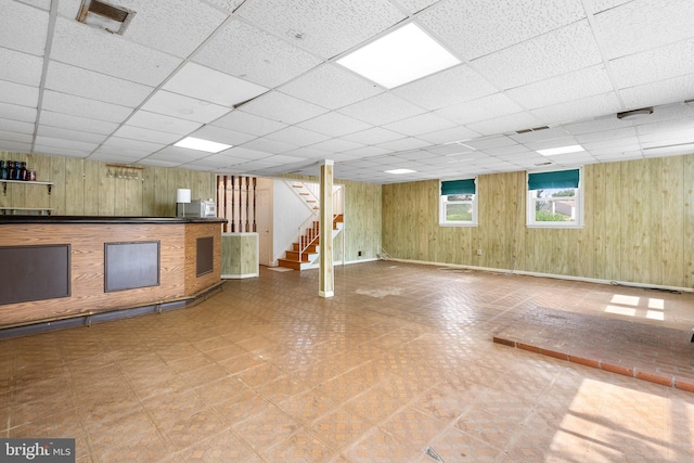 below grade area with wood walls, a drop ceiling, stairs, and tile patterned floors