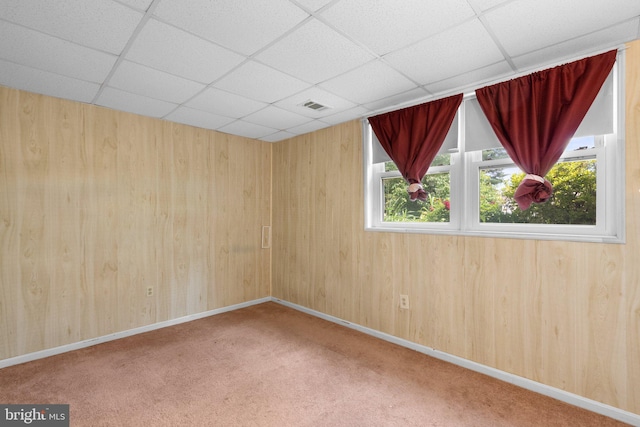 unfurnished room featuring a drop ceiling, carpet flooring, wood walls, and baseboards