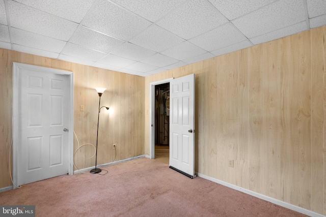 unfurnished bedroom with wooden walls, carpet, baseboards, and a paneled ceiling
