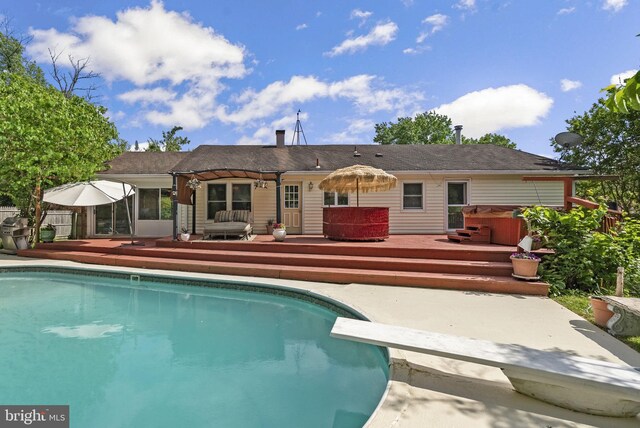 rear view of house featuring a hot tub, a wooden deck, an outdoor pool, and a patio