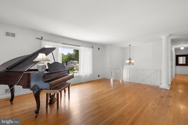 living area featuring light wood-style floors, a chandelier, decorative columns, and baseboards