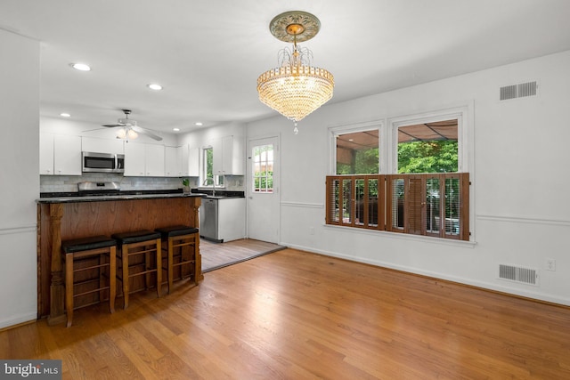 kitchen with stainless steel appliances, dark countertops, white cabinets, light wood-style floors, and backsplash