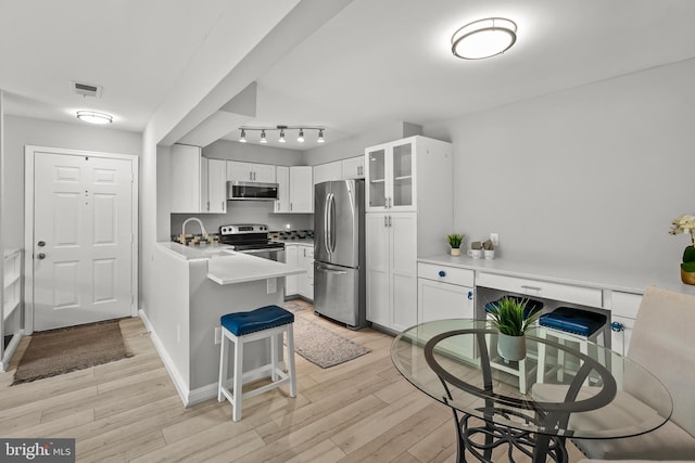 2224 Springwood Dr Unit 102A, Reston, VA 20191 - kitchen with appliances with stainless steel finishes, a peninsula, light wood-style flooring, white cabinetry, and glass insert cabinets