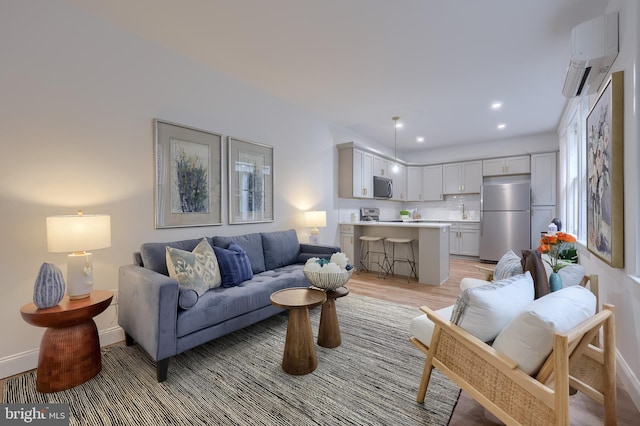 living room featuring a wall mounted AC, light wood-style flooring, recessed lighting, and baseboards