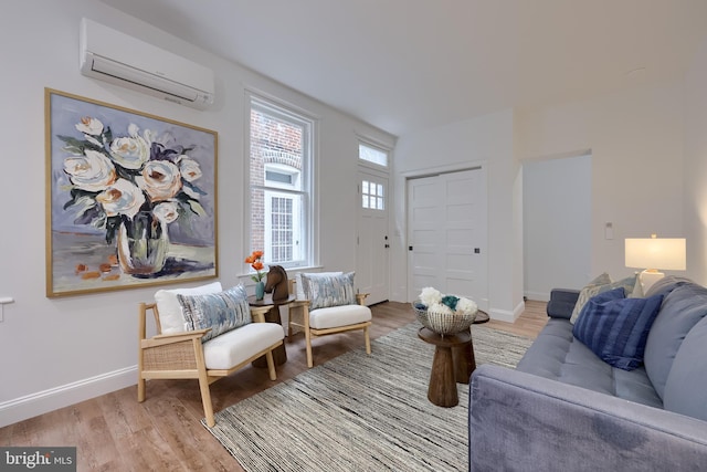 living room featuring a wall mounted air conditioner, light wood finished floors, and baseboards
