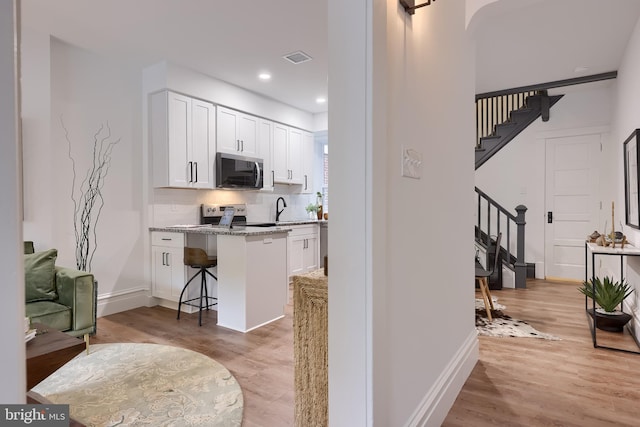 kitchen with white cabinetry, a kitchen bar, backsplash, light wood-type flooring, and light stone counters
