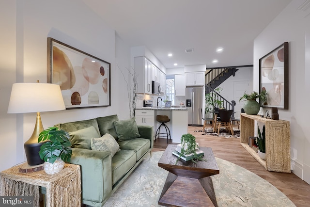 living area featuring light wood finished floors, recessed lighting, and stairs