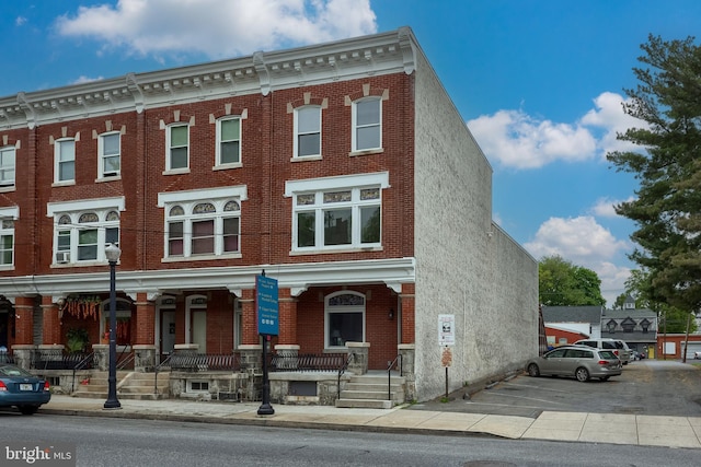 townhome / multi-family property featuring brick siding, covered porch, and uncovered parking