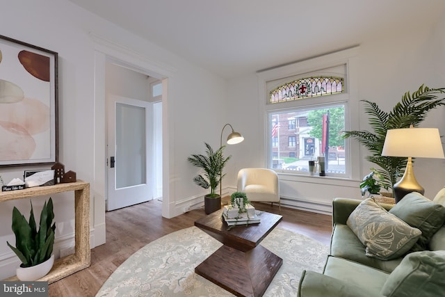 living area with a baseboard heating unit, wood finished floors, and baseboards