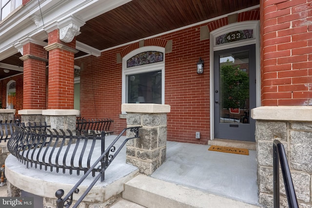 doorway to property featuring covered porch and brick siding