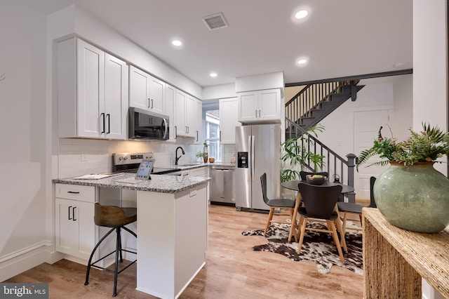 kitchen featuring stainless steel appliances, a peninsula, a sink, light stone countertops, and light wood-type flooring