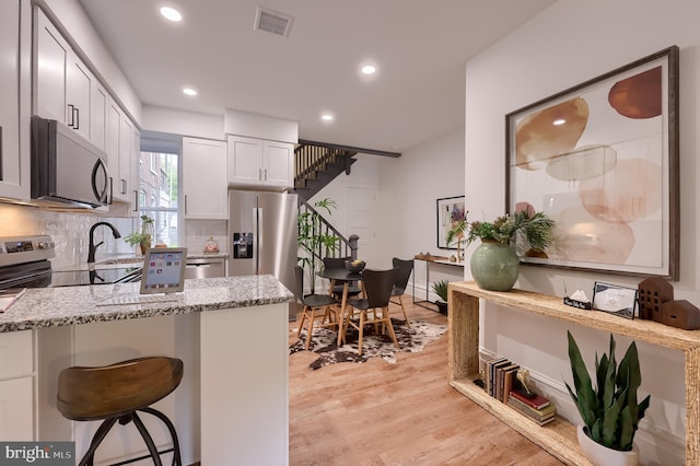 kitchen featuring appliances with stainless steel finishes, light stone counters, recessed lighting, a kitchen bar, and tasteful backsplash
