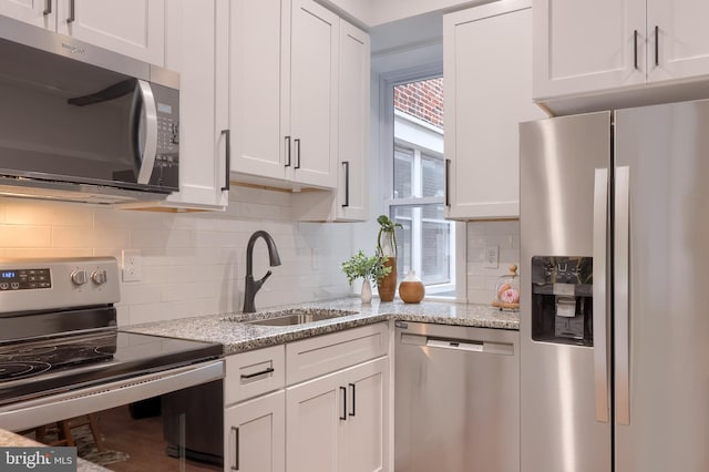 kitchen with stainless steel appliances, a sink, white cabinets, decorative backsplash, and light stone counters