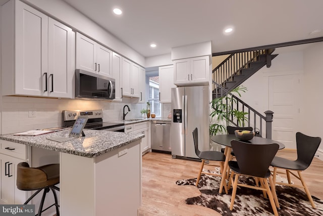 kitchen featuring appliances with stainless steel finishes, a peninsula, light stone counters, a sink, and white cabinets
