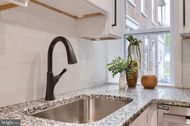kitchen view of a sink, white cabinetry, tasteful backsplash, and light stone counters