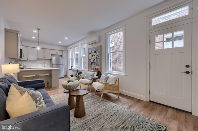 living area featuring a wall mounted AC, light wood-style flooring, baseboards, and recessed lighting