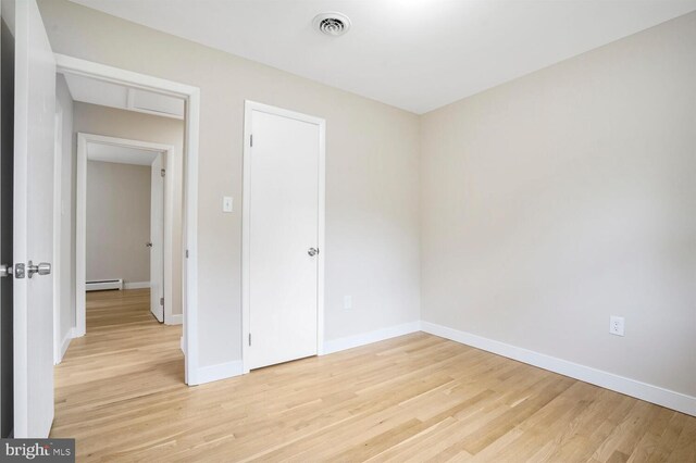 spare room with a baseboard radiator, light wood-style floors, and baseboards