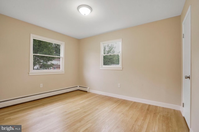 empty room featuring a baseboard heating unit, light wood-style flooring, and baseboards