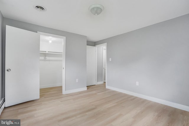 unfurnished bedroom featuring light wood finished floors, baseboards, a walk in closet, and a closet