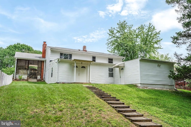 back of house featuring a chimney, a yard, and a sunroom