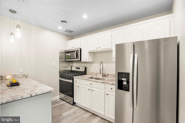kitchen with stainless steel appliances, a sink, light wood-style floors, light stone countertops, and white cabinetry